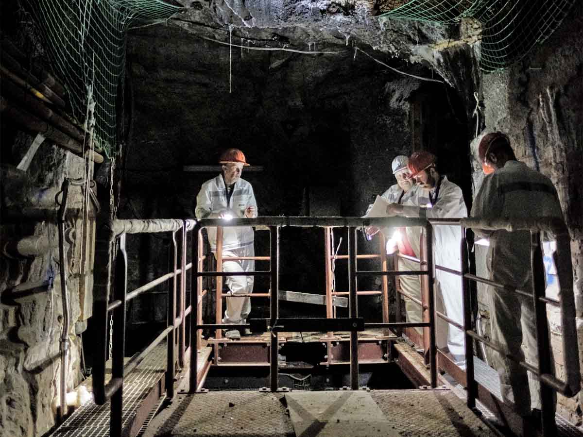 Personen in weißen Schutzanzügen auf einer Arbeitsbühne unter Tage