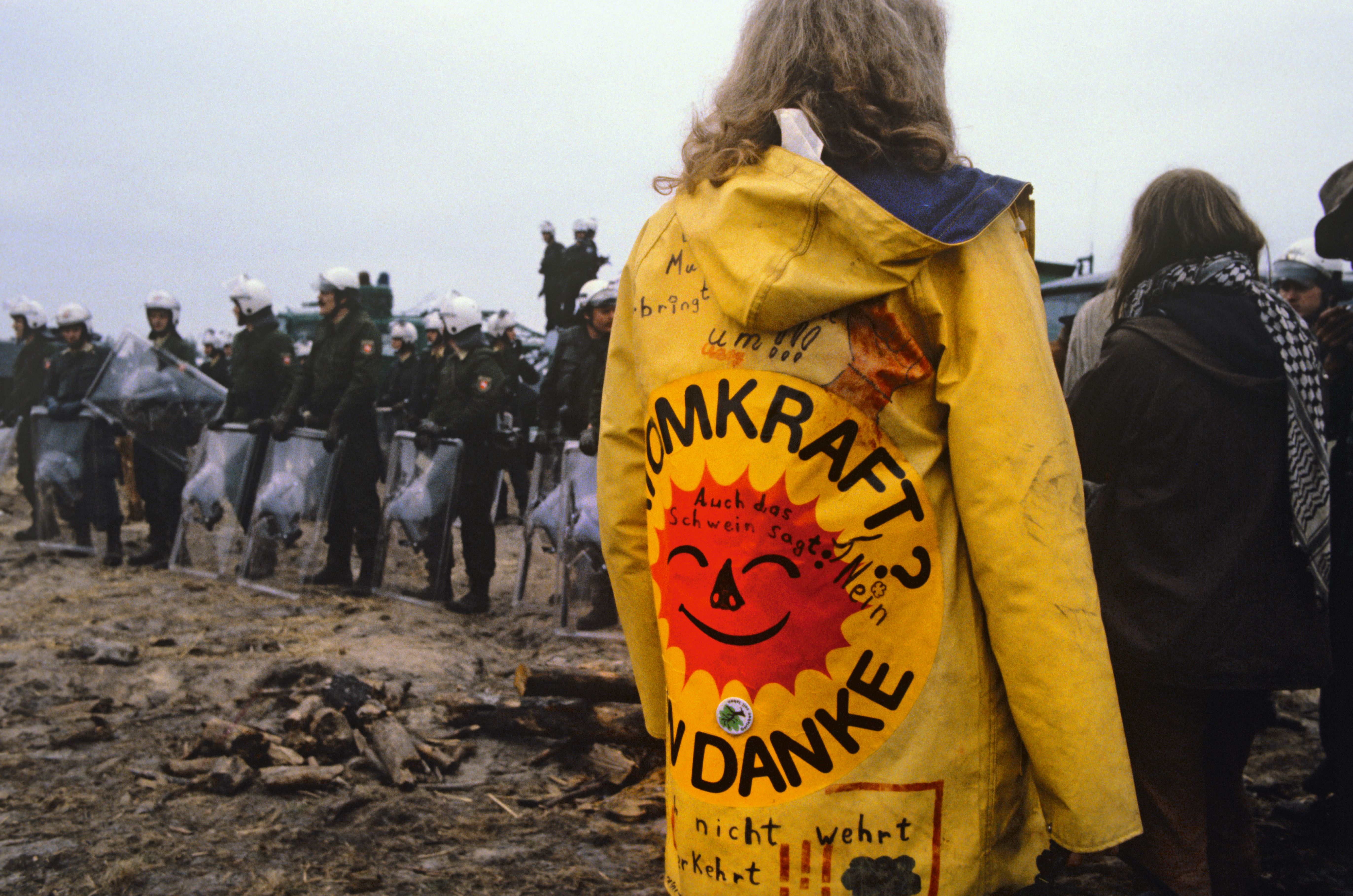 Person mit Jacke, auf der das "Atomkraft? Nein danke!"-Zeichen zu erkennen ist. Weitere Personen und Polizisten im Hintergrund.